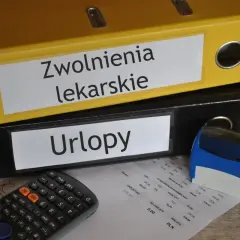 Segregator "Zwolnienia lekarskie" i "Urlopy" obok kalkulatora i pieczątki. Dokumenty mogą zawierać kod choroby a.