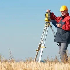 Geodeta w żółtym kasku i kurtce pracuje z niwelatorem, ustalając, ile bierze geodeta za wytyczenie działki.