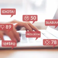 Dłonie piszą na klawiaturze, otoczone dymkami z obraźliwymi komentarzami: "IDIOTA!", "SŁABIAK", "PRZEGRYW", "!-@#$@". To przykład naruszenia dóbr osobistych w sieci.