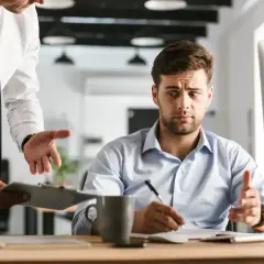 Szef z wyrzutem patrzy na pracownika, który tłumaczy swoją nieobecność w pracy.