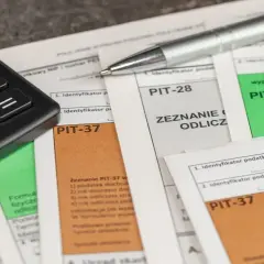 Kalkulator i długopis leżą na formularzach PIT-37, PIT-28 i PIT-36. Czas obliczyć, ile wynosi podatek dochodowy.