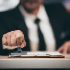 Biznesmen pieczętuje dokumenty, a klepsydra symbolizuje upływ czasu. To może być związane z tym, kompensata co to.