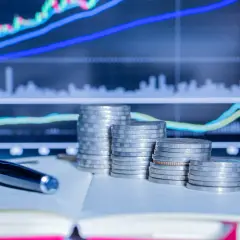 Stosy monet i długopis na tle wykresów giełdowych. Planowanie finansowe i rezydencja podatkowa w Polsce.