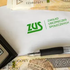 Kalkulator, długopis i pieniądze leżą obok koperty z logo ZUS. Temat: dziedziczenie składek ZUS.
