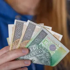 Dłoń trzyma polskie banknoty 100 i 200 zł. To symbol dodatku za wysługę lat w budżetówce.