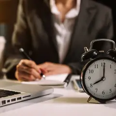 Budzik pokazuje 8:00, a osoba pisze w notatniku. To znak, że maj ilosc godzin pracy dopiero się zaczyna.