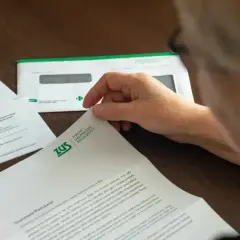 Osoba przegląda dokument ZUS. Może to być informacja o zwrocie nadpłaty lub inne pismo z ubezpieczalni.