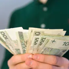 Dłonie trzymają plik banknotów 100 zł. To może być pomocne przy pytaniu, co to jest renta rodzinna.