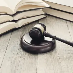 Młotek sędziowski i otwarte księgi na drewnianym stole. Symbolizują prawo, sprawiedliwość i procesy, jak umowa cesji wierzytelności.