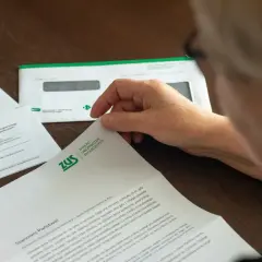 Osoba przegląda dokumenty ZUS, sprawdzając saldo ma zus. Widać kopertę i pisma dotyczące ubezpieczeń.