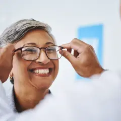 Uśmiechnięta kobieta przymierza okulary, które mogą być objęte refundacją okularów przez pracodawcę.