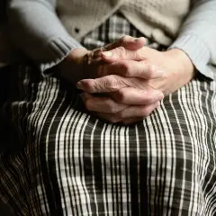 Dłonie starszej osoby splecione na sukience w kratę. Wzór umowy darowizny bez notariusza.