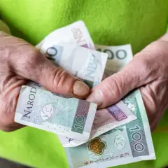 Dłonie trzymają polskie banknoty. Zmiany w nowych zasadach przyznawania renty socjalnej mogą wpłynąć na finanse.
