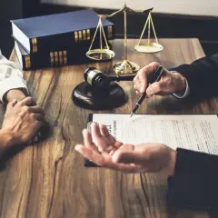 Prawnik omawia z klientem dokumenty, wskazując piórem na umowę. W tle waga sprawiedliwości i księgi. To ważny moment, by złożyć list intencyjny praca.