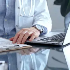 Lekarz w białym kitlu pisze na dokumentach, obok laptop. Zastanawia się, ile można być na zwolnieniu lekarskim od psychiatry.