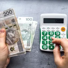 Dłoń trzyma banknoty 200 zł i 100 zł, obok kalkulator z wyświetloną kwotą 50000. Może to być podstawa do obliczenia składek ZUS, np. kod 0590.