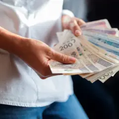 Dłonie trzymające plik banknotów. Wartość najniższej krajowej brutto jest tematem dyskusji, a pieniądze symbolizują zarobki.