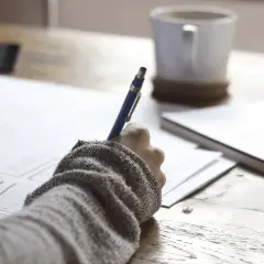 Ręka pisze na papierze, obok kubek kawy. Może to być notatka o zus zfa co to jest.