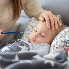 Czuła opieka na dziecko podczas choroby. Mama mierzy gorączkę, głaszcze po czole. Obok leki.