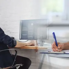 Mężczyzna pracuje przy komputerze, podczas gdy lekarz wypełnia dokumenty. Czy na L4 można pracować? To pytanie nurtuje wielu.