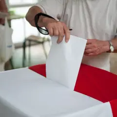 Mężczyzna wrzuca kartę do urny. Dowiedz się, jak głosować poza miejscem zamieszkania, aby Twój głos się liczył.