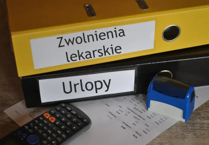 Segregator "Zwolnienia lekarskie" i "Urlopy" obok kalkulatora i pieczątki. Dokumenty mogą zawierać kod choroby a.