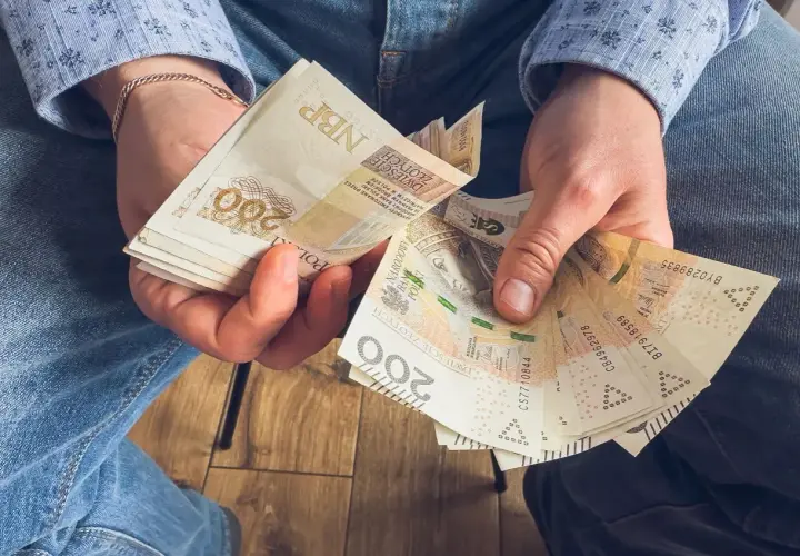 Ręce trzymające stos banknotów 200 zł. To może być wynagrodzenie za urlop, które pozwoli na zasłużony odpoczynek.