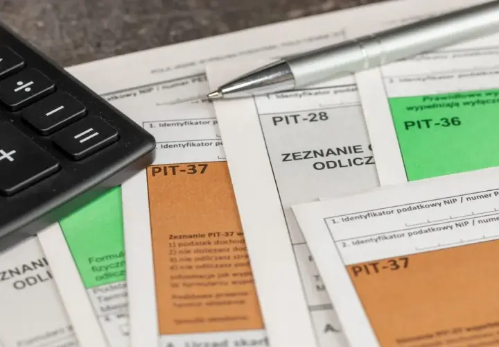Kalkulator i długopis leżą na formularzach PIT-37, PIT-28 i PIT-36. Czas obliczyć, ile wynosi podatek dochodowy.