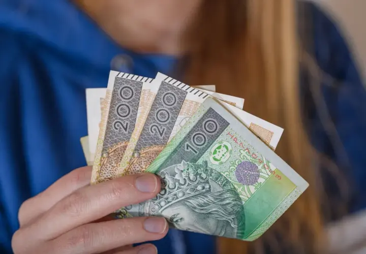 Dłoń trzyma polskie banknoty 100 i 200 zł. To symbol dodatku za wysługę lat w budżetówce.