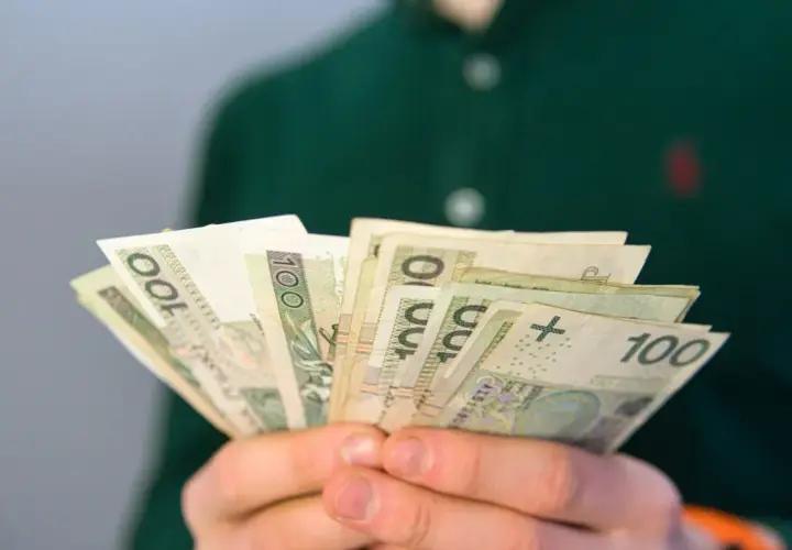 Dłonie trzymają plik banknotów 100 zł. To może być pomocne przy pytaniu, co to jest renta rodzinna.