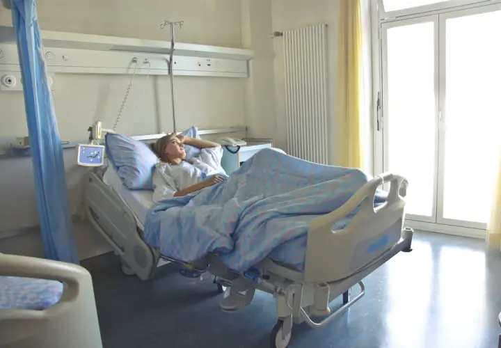Pacjentka w szpitalnym łóżku, zastanawia się, zwolnienie lekarskie ile płatne. Jasne okno i zasłony.