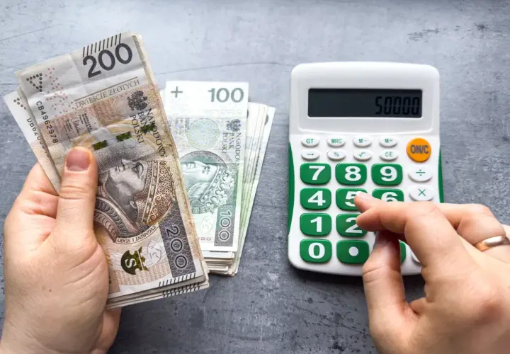 Dłoń trzyma banknoty 200 zł i 100 zł, obok kalkulator z wyświetloną kwotą 50000. Może to być podstawa do obliczenia składek ZUS, np. kod 0590.