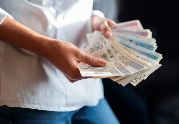 Dłonie trzymające plik banknotów. Wartość najniższej krajowej brutto jest tematem dyskusji, a pieniądze symbolizują zarobki.