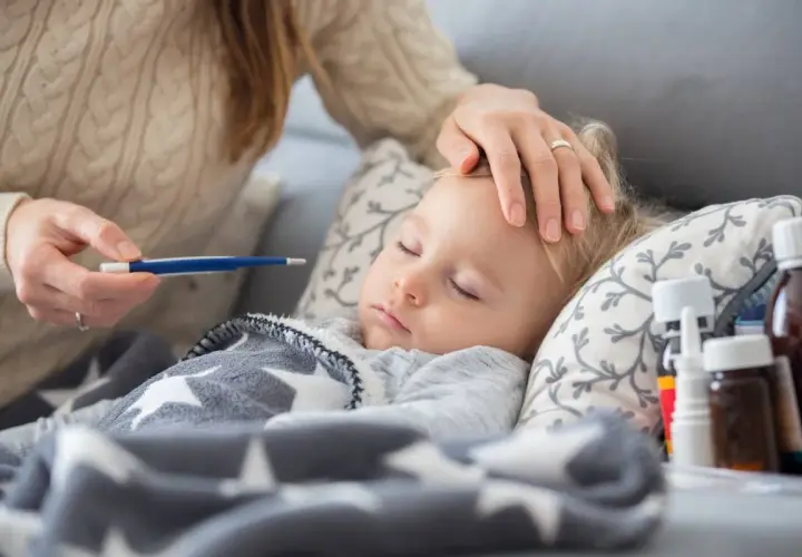 Czuła opieka na dziecko podczas choroby. Mama mierzy gorączkę, głaszcze po czole. Obok leki.
