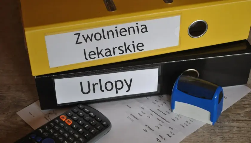Segregator "Zwolnienia lekarskie" i "Urlopy" obok kalkulatora i pieczątki. Dokumenty mogą zawierać kod choroby a.