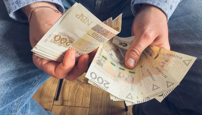 Ręce trzymające stos banknotów 200 zł. To może być wynagrodzenie za urlop, które pozwoli na zasłużony odpoczynek.