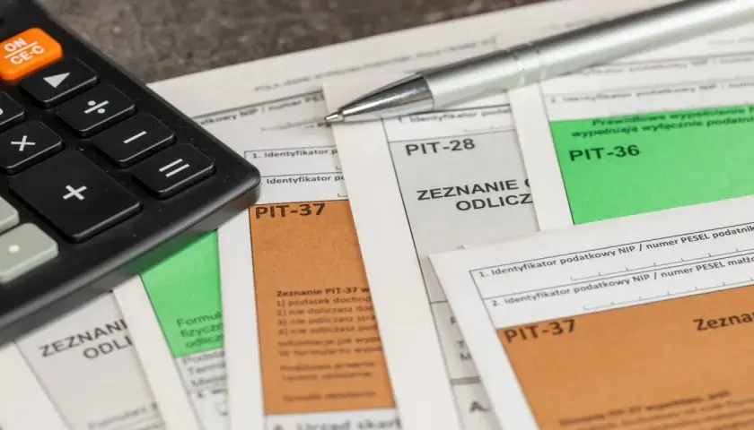 Kalkulator i długopis leżą na formularzach PIT-37, PIT-28 i PIT-36. Czas obliczyć, ile wynosi podatek dochodowy.