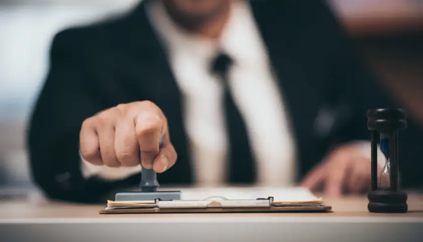 Biznesmen pieczętuje dokumenty, a klepsydra symbolizuje upływ czasu. To może być związane z tym, kompensata co to.