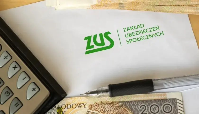 Kalkulator, długopis i pieniądze leżą obok koperty z logo ZUS. Temat: dziedziczenie składek ZUS.