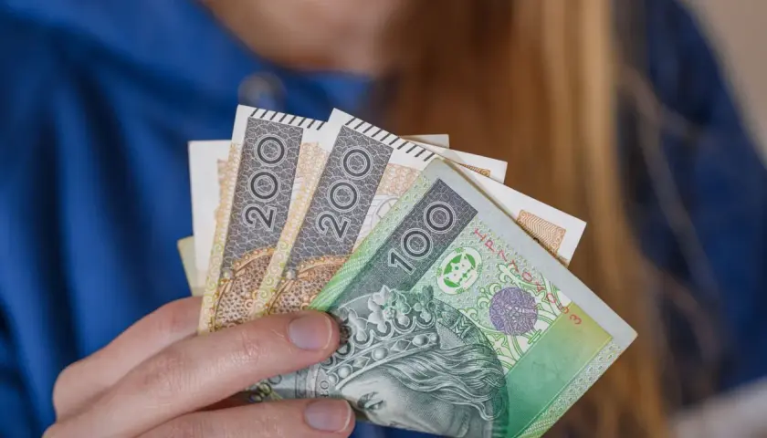 Dłoń trzyma polskie banknoty 100 i 200 zł. To symbol dodatku za wysługę lat w budżetówce.