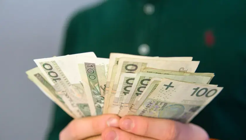 Dłonie trzymają plik banknotów 100 zł. To może być pomocne przy pytaniu, co to jest renta rodzinna.