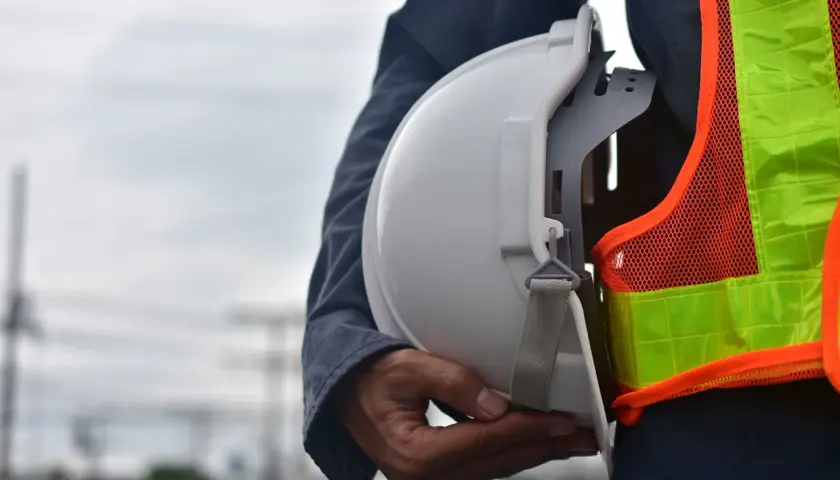 Pracownik budowlany trzyma biały kask. Kamizelka odblaskowa sugeruje, że to przykład sytuacji, która może prowadzić do zwolnienia dyscyplinarnego.