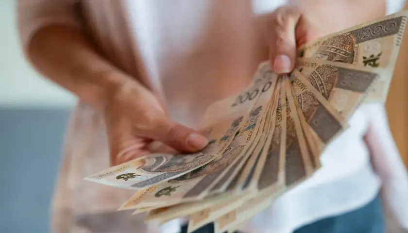 Dłonie trzymają wachlarz banknotów 200 zł. To nagroda za długoletni jubileusz w pracy.