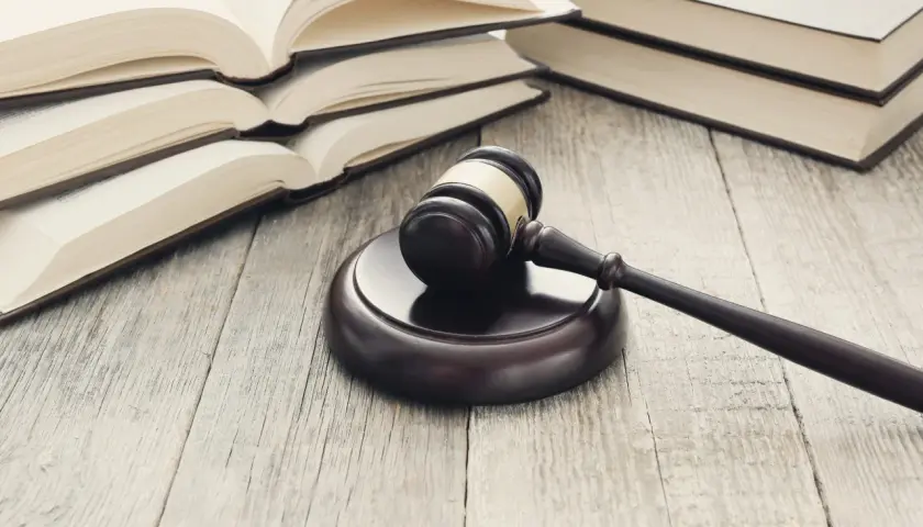 Młotek sędziowski i otwarte księgi na drewnianym stole. Symbolizują prawo, sprawiedliwość i procesy, jak umowa cesji wierzytelności.