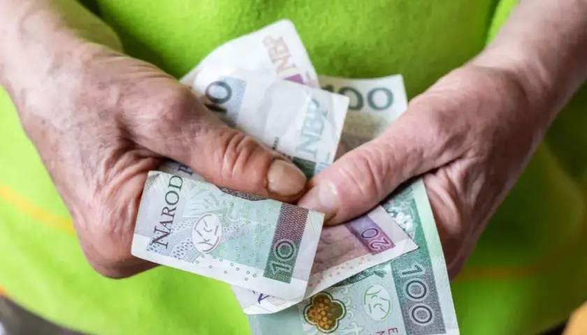 Dłonie trzymają polskie banknoty. Zmiany w nowych zasadach przyznawania renty socjalnej mogą wpłynąć na finanse.