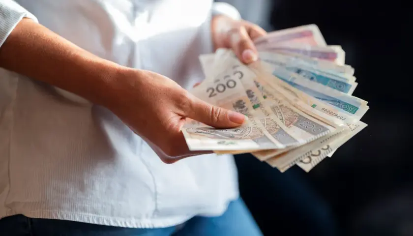 Dłonie trzymające plik banknotów. Wartość najniższej krajowej brutto jest tematem dyskusji, a pieniądze symbolizują zarobki.
