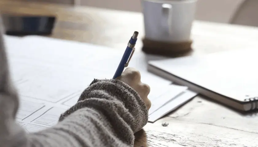 Ręka pisze na papierze, obok kubek kawy. Może to być notatka o zus zfa co to jest.