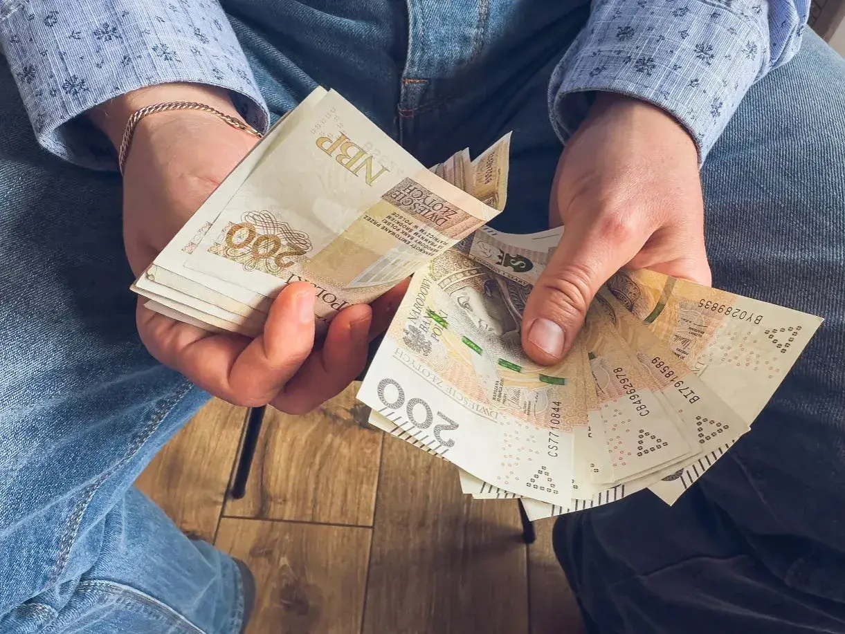 Ręce trzymające stos banknotów 200 zł. To może być wynagrodzenie za urlop, które pozwoli na zasłużony odpoczynek.