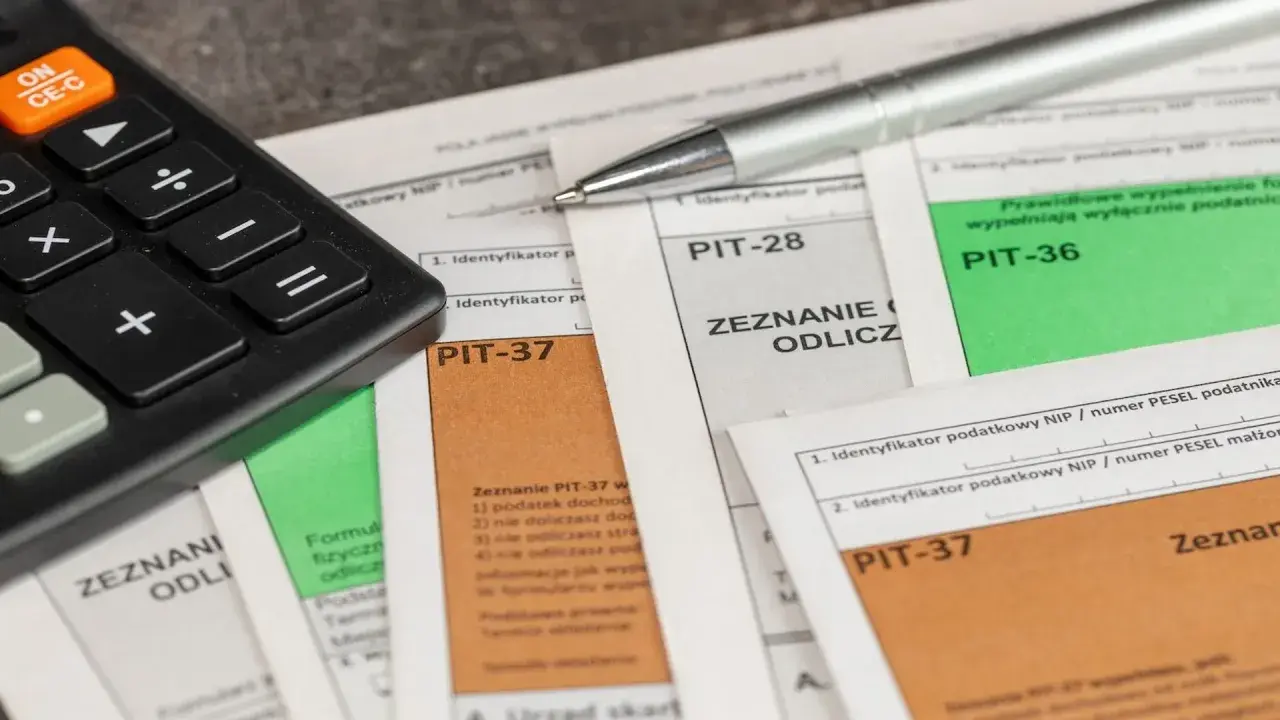 Kalkulator i długopis leżą na formularzach PIT-37, PIT-28 i PIT-36. Czas obliczyć, ile wynosi podatek dochodowy.