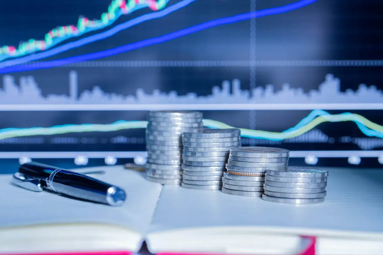 Stosy monet i długopis na tle wykresów giełdowych. Planowanie finansowe i rezydencja podatkowa w Polsce.